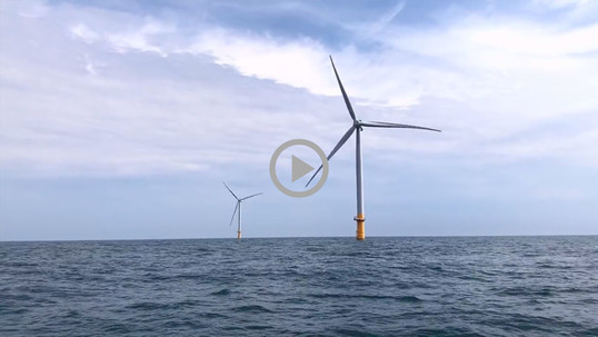 Two wind turbines on the ocean in front of a blue sky