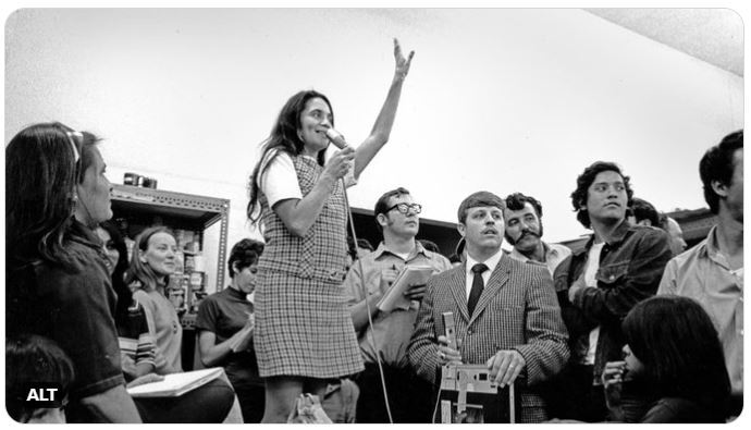Labor and civil rights activist Dolores Huerta speaks at a microphone in front of a crowd of supporters. 