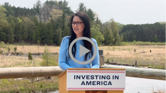 Assistant Secretary for Fish and Wildlife and Parks Shannon Estenoz speaks at an outdoor podium hung with the sign “Investing in America.”