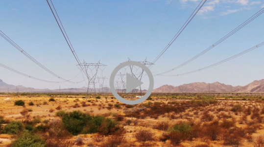 Power lines run from power transmission towers across a desert landscape.