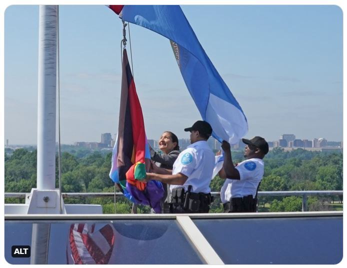 Secretary Haaland and building facility staff raise Progress Pride flag on the rooftop of the Stewart Lee Udall Building.