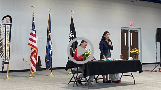 Secretary Haaland stands with a microphone next to a seated Assistant Secretary for Indian Affairs Bryan Newland in a Tribal auditorium in Minnesota.