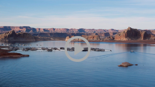 A view of Lake Mead in slanting afternoon light, boats float on the water under a blue sky.