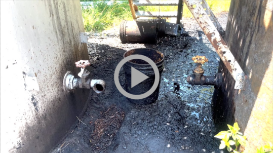 Oil residue soaks the ground between two rusting storage tanks.