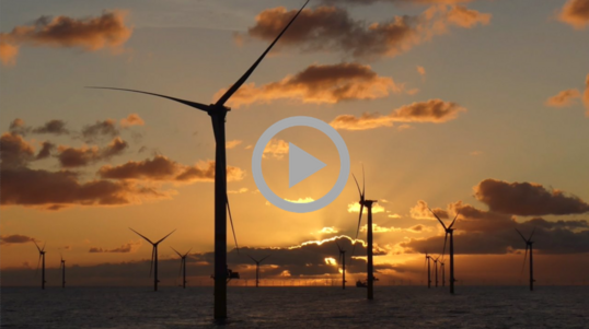 A view of ocean wind turbines against the sky at sunset.