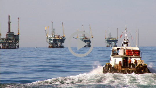 A boat makes it way toward four offshore oil rigs.