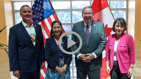 Secretary Haaland, Assistant Secretary Carmen Cantor and Assistant Secretary Bryan Newland pose in front of the U.S and Canada flags.  