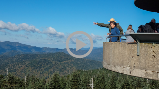From a lookout tower, a National Park Service park ranger points and shows Secretary Haaland something off in the distance. 