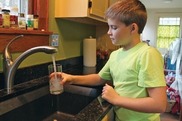 Child filling a glass of water at a sink