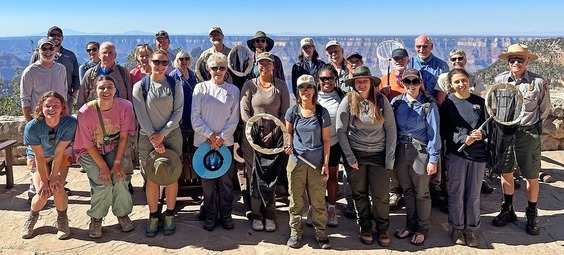 a group of smiling people holding butterfly nets on the rim of the Grand Canyon