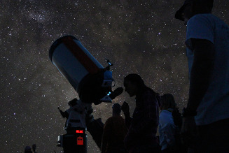 a group of people looking through a telescope at a starry night sky