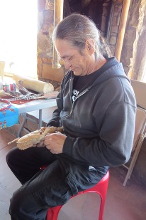 a man sitting in a chair carving a piece of wood