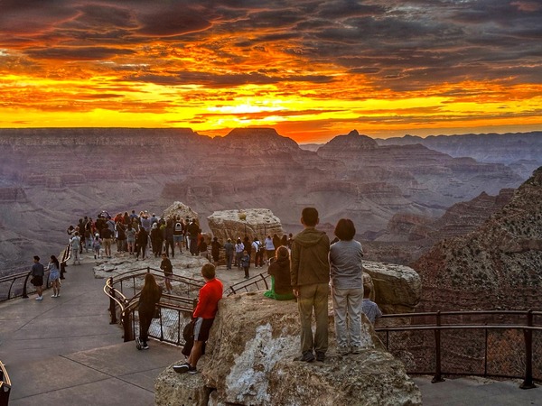 a group of people standing at an overlook on the rim of a canyon during sunrise