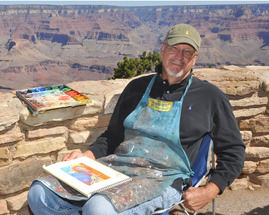 a man in a paint-splattered apron next to an easel on the rim of a large canyon