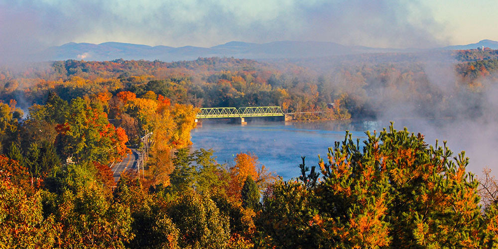 A view of the Champlain Canal in fall with colorful foliage and mist on the water.