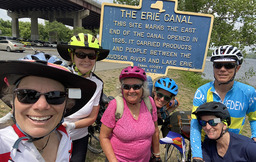 A group of cyclists have their picture taken next to a historic marker for the Erie Canal.