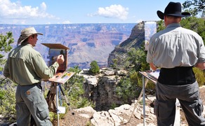 two men painting on the rim of a large desert canyon
