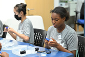 Two students press their thumbs into blue silly putty during an education program on fingerprinting. 