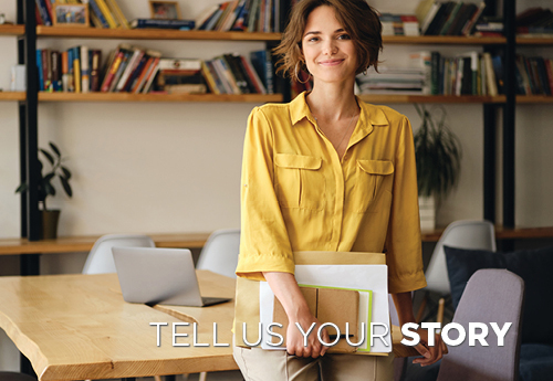 Tell Us Your Story woman in yellow shirt standing in front of bookshelf