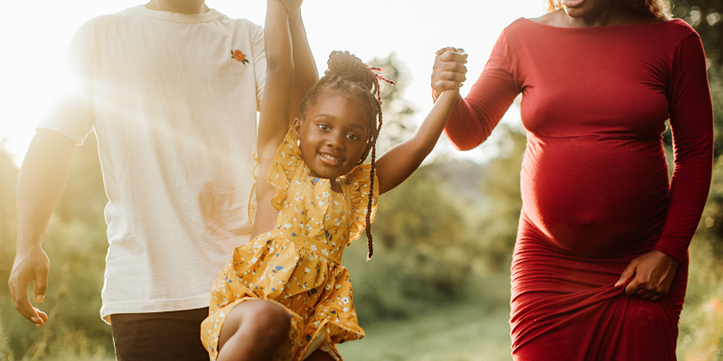 Pregnant woman lifts smiling child into the air