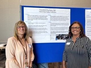 Pictured: Louise Bachand (left) and Wanda Dyer (right) standing in front of a blue presentation board. 