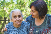 A middle-aged person puts their arm around an elderly person, standing outdoors.