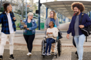 A diverse group of four young adults make their way together down a wide cobbled walkway in a campus-like setting. 