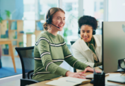 Two coworkers using headsets and working at computers in an office setting.