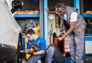 An apprentice with a disability works on a car in an auto body workshop under the guidance of an instructor.