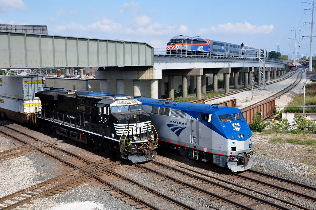 Two trains moving under a trestle with another approaching the trestle above.
