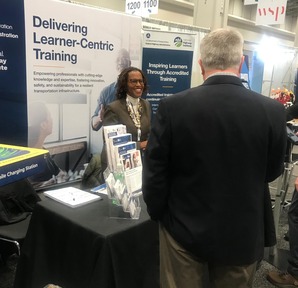 NHI Director Stacey Caston talks with a TRB Annual Meeting male attendee at the NHI booth filled with flyers.