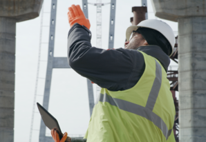 Male civil engineer wearing a yellow vest and hard hat gesturing towards the sky during bridge construction