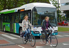 People riding bikes on a city street with traffic, including a bus.