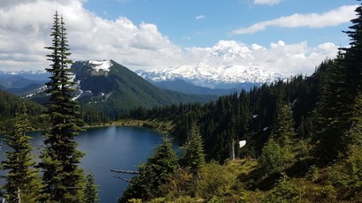 Tall mountain in the background with trees and a small lake in the foreground. 