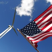 An American flag and a wind turbine against a blue sky.