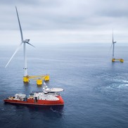 Photo of three offshore wind turbines with two ships in the foreground.