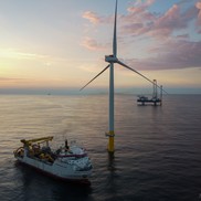 An offshore wind turbine in a calm ocean with a service vessel nearby.