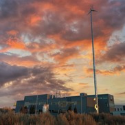 Small wind turbine stands beside a building at sunset.