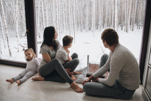 A family looking out a window at snow on the ground.