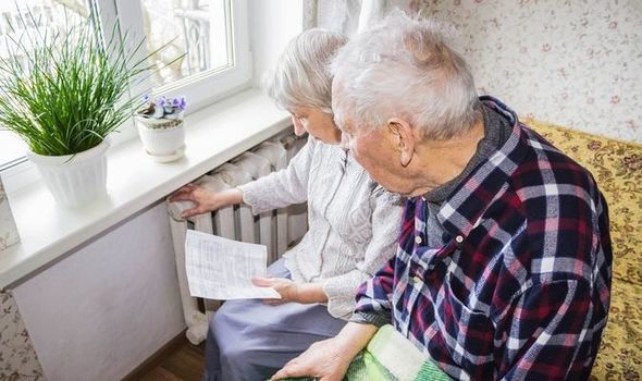 An elderly couple sitting by a radiator examining a bill.
