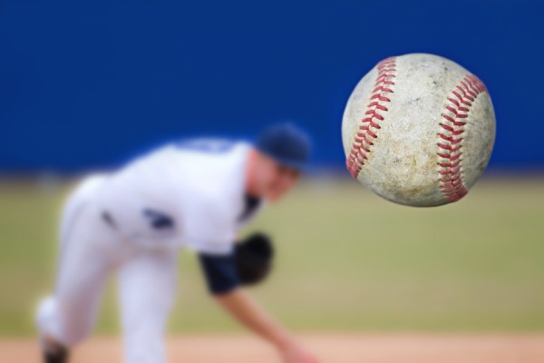 Closeup of a baseball thrown by a player in the background