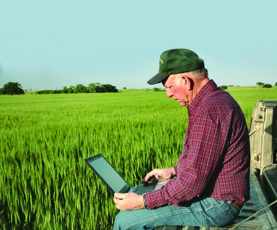 Man sitting on a vehicle in a field, .looking at a computer