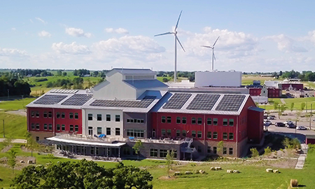 A school with solar panels on the roof and a distributed wind turbine in the background.