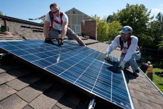 Two workers installing solar panels on the roof of home.