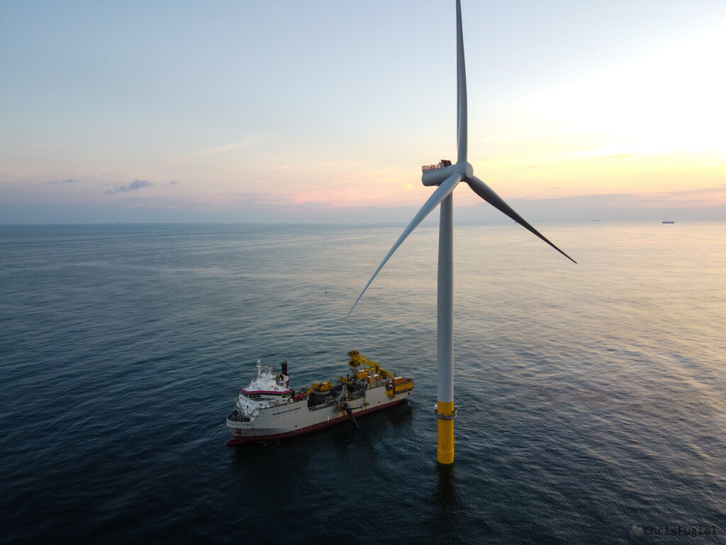 A wind turbine installation vessel floats next to a wind turbine in a large body of water. 