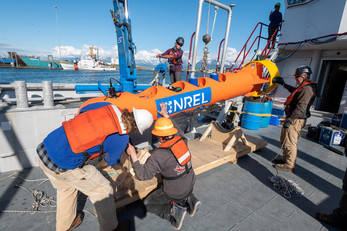 People in hard hats and life vests on a dock adjusting a cylindrical buoy stamped with the NREL logo.