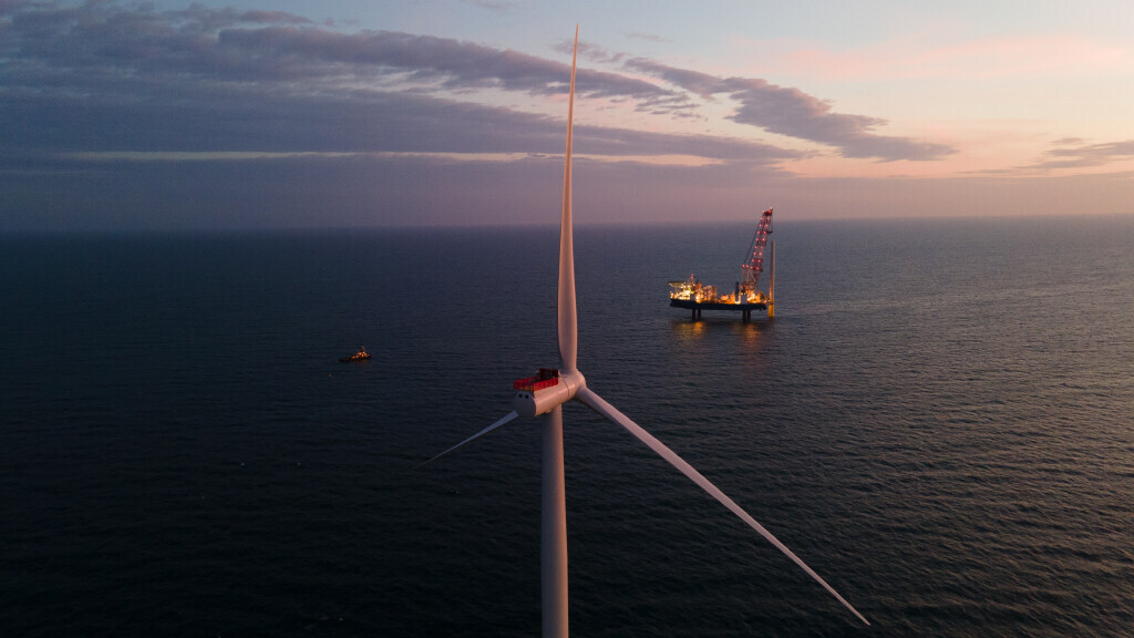 A view from behind an ocean-bound wind turbine with an installation boat and smaller safety boat on the horizon.