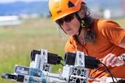 Shari Matzner in a hard hat and sunglasses operating equipment on a grassy plain.