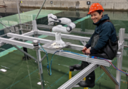 Oregon State University graduate student Akiri Seki sits next to a robotic arm attached to a small-scale floating offshore wind energy platform.