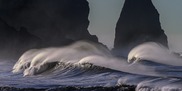 Waves crash on a rocky shoreline, with large cliffs in the distance